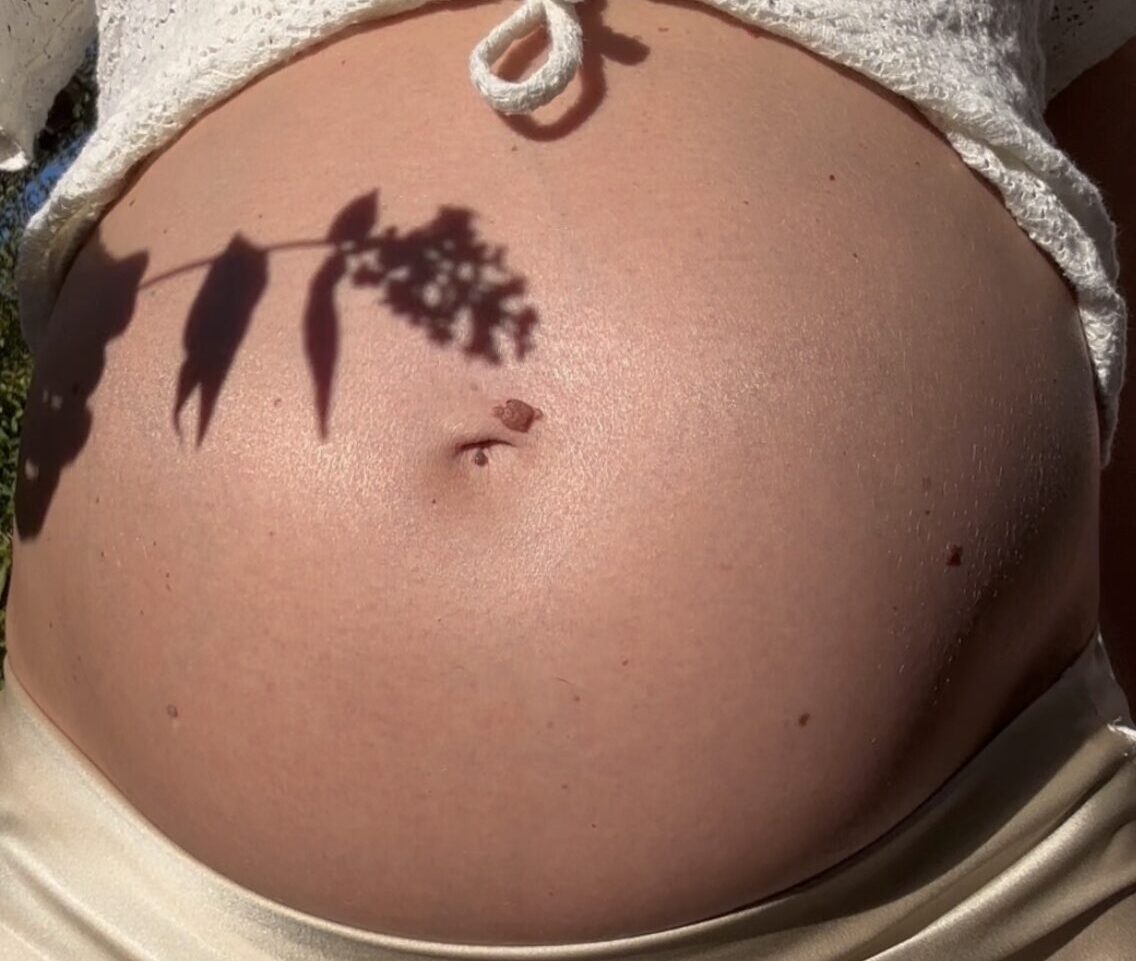 Schwangerer Bauch in der Sonne, darauf der Schatten eines Zweiges.